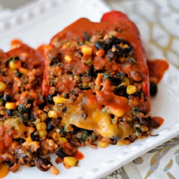 Two stuffed peppers with melted cheese and enchilada sauce on a plate.