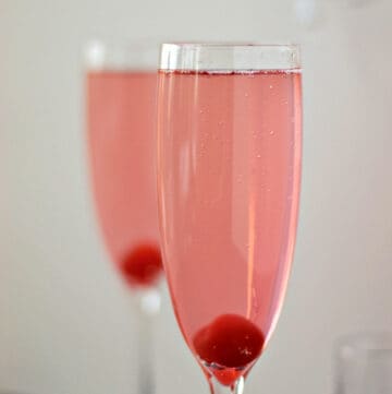 Two pink, sparkling cocktails with a cherry at the bottom of a champagne flute.