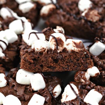 A single chocolate brownie topped with melted chocolate and mini marshmallows resting on top of a platter full of brownies.