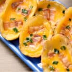 potato skins topped with bacon and green onions spread out on a rectangle blue plate