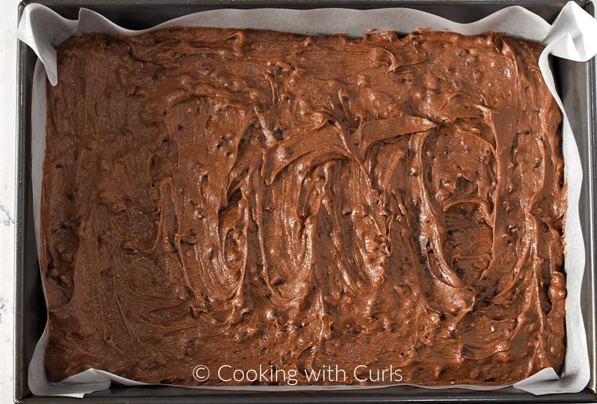 Brownie batter spread out in a parchment paper lined baking pan. 