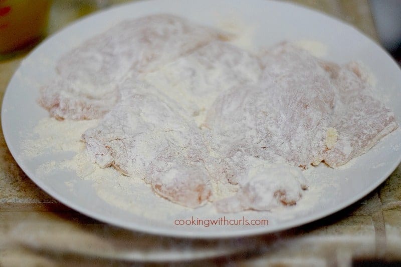 flattened chicken pieces dredged in flour on a large white plate