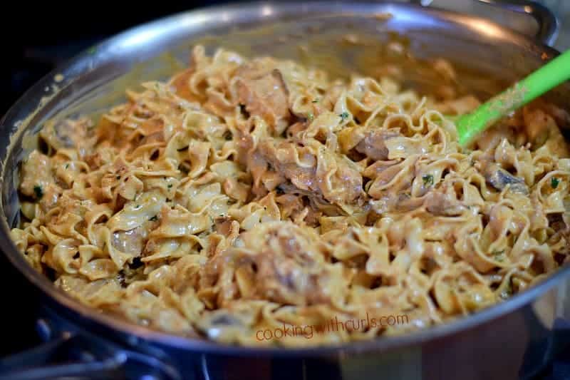a large stainless steel skillet with Chicken Paprikash being tossed with Noodles and a green spoon in the upper right hand side