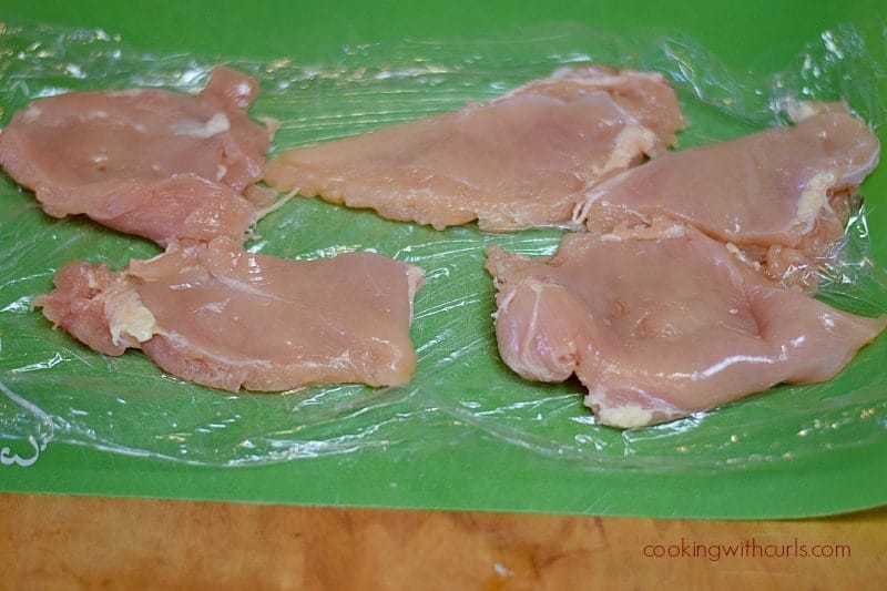 two chicken breasts cut into four pieces on a green cutting mat