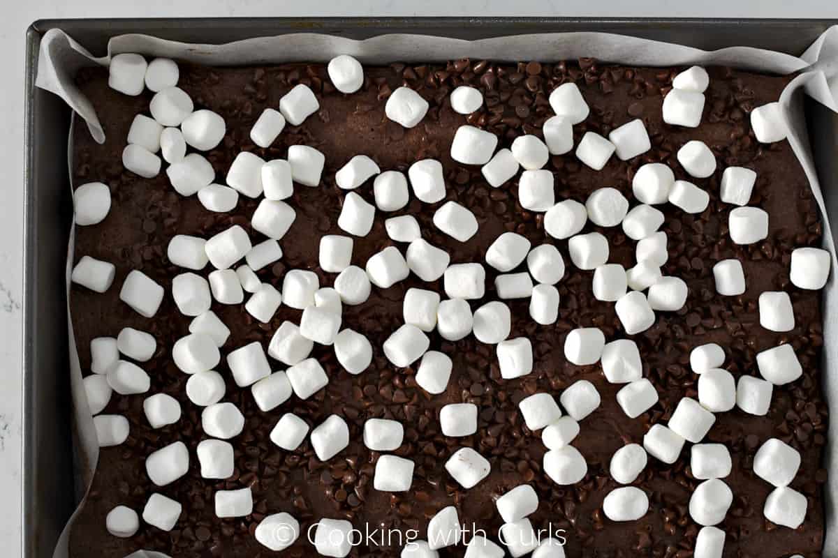 Chocolate chips and mini marshmallows on top of baked brownies in a baking pan. 