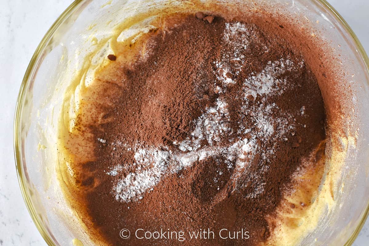 Cocoa powder and flour on top of the butter sugar mixture in a mixing bowl. 