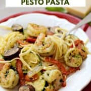 Pesto shrimp, bell pepper, zucchini, mushrooms and pasta on a plate with a wedge of parmesan in the background and title graphic across the top.