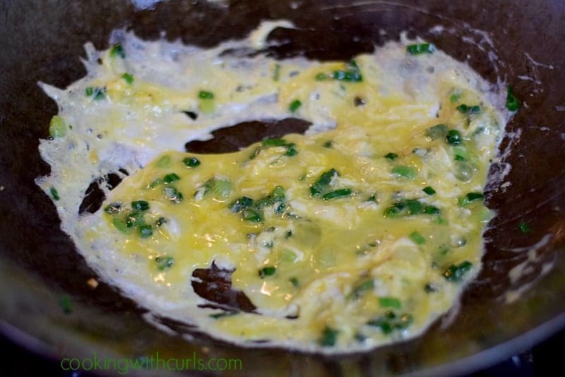 Raw scrambled eggs added to the green onions and garlic in a wok.