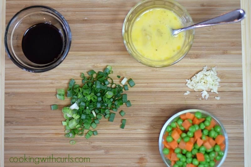 Soy sauce, peas and carrots, scrambled eggs in glass bowls, with chopped green onions and garlic on the side.