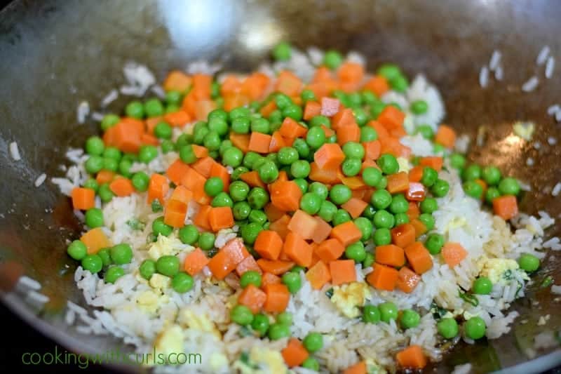 Peas and carrots on top of the rice and egg mixture in the wok.