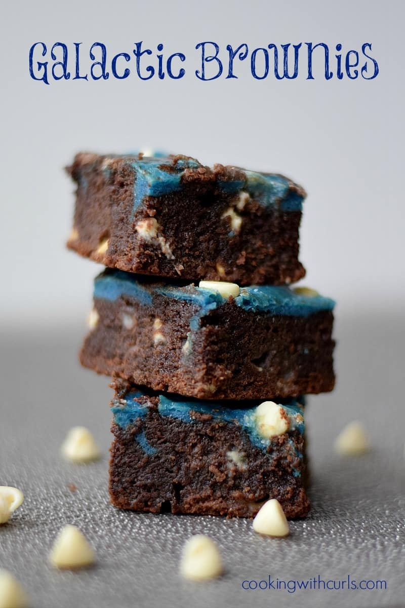 Three blue swirled galactic brownies stacked on top of each other surrounded by white chocolate chips.