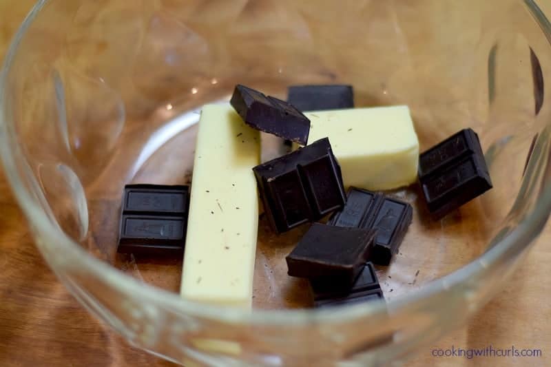 Two sticks of butter and broken pieces of dark chocolate in a large bowl.