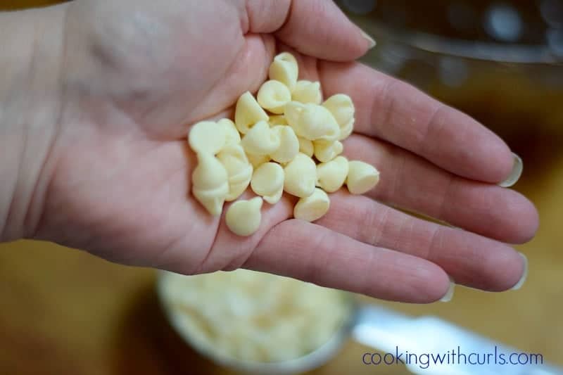 A woman's hand holding a scoop of white chocolate chips.