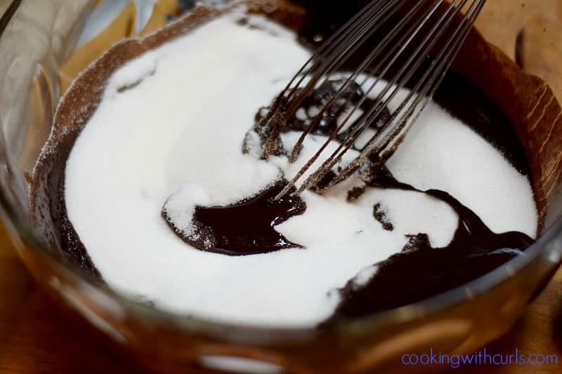 Sugar being whisked into the melted chocolate mixture in a large mixing bowl.