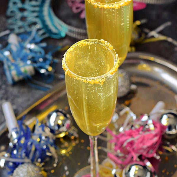 Two champagne glasses filled with gold cocktail surrounded by party hats and streamers.