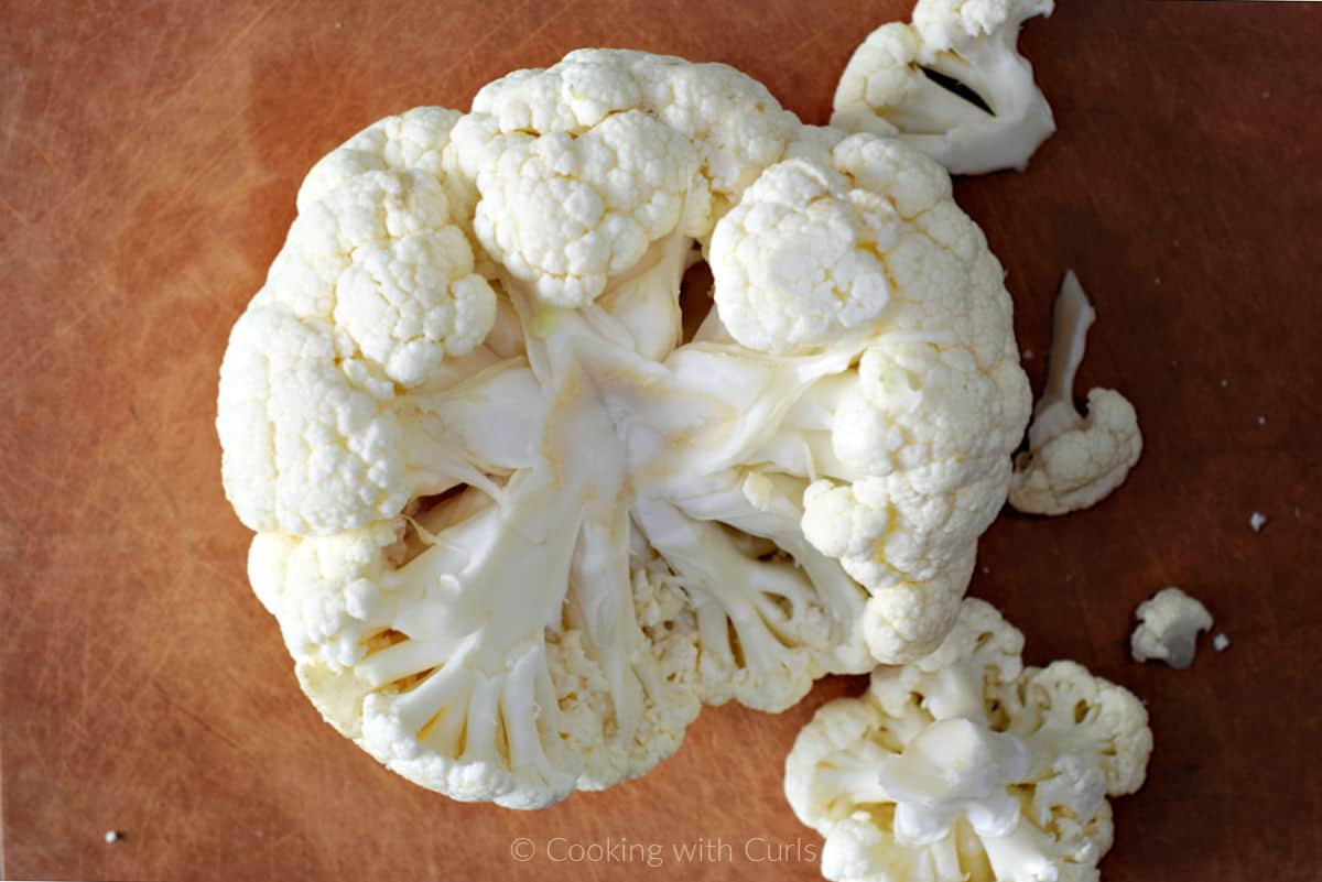 Head of cauliflower on cutting board with stem and leaves removed.