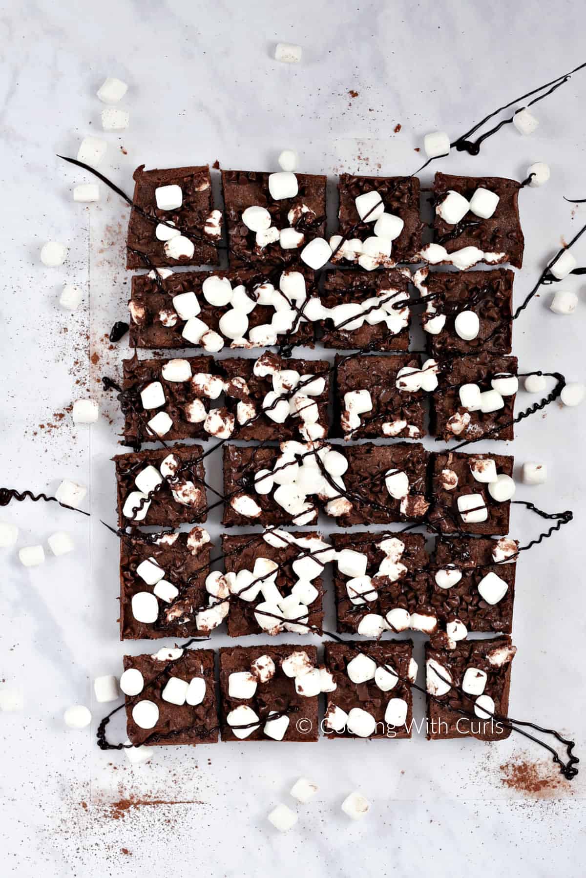 Looking down on twenty four brownie squares  topped with mini marshmallows and drizzled with chocolate. 