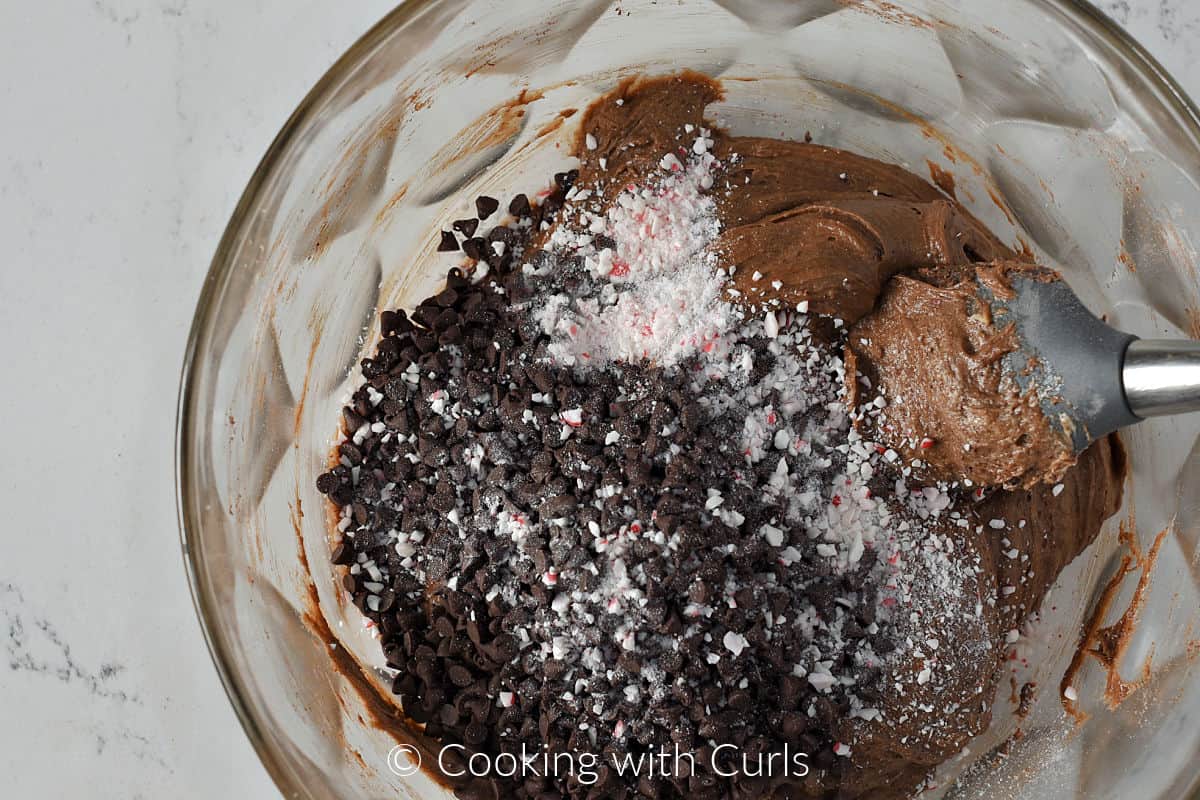 Mini chocolate chips and crushed candy cane in a mixing bowl with brownie batter. 