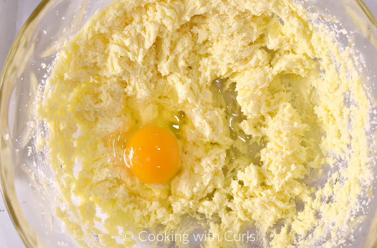 One egg on top of beaten sugar and butter mixture in a mixing bowl. 