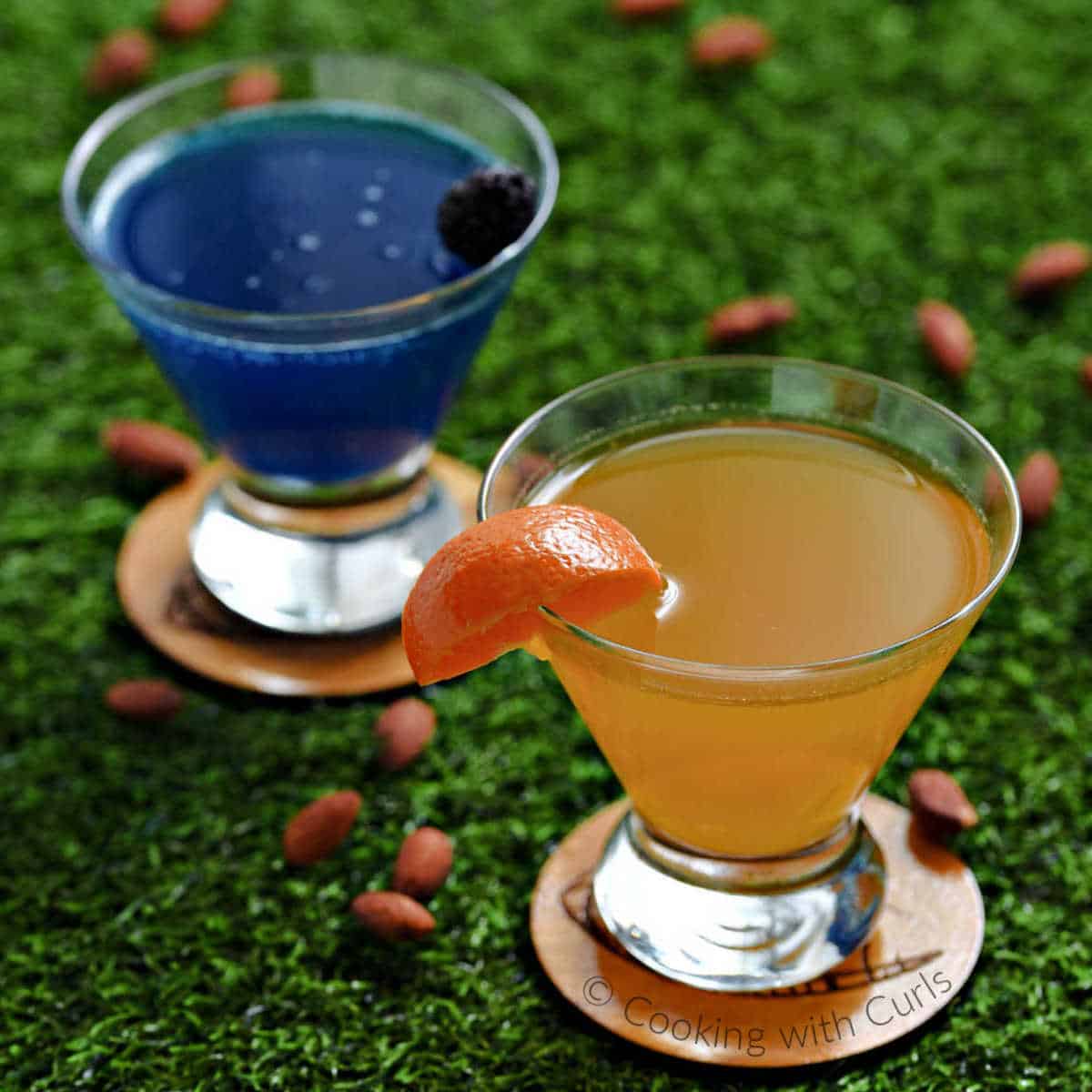 a dark blue martini and an orange martini on green grass.
