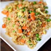 Rice mixed with soy sauce, scrambled eggs, peas, carrots, and green onions on a square plate.