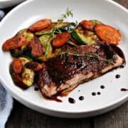 Cherry chipotle glazed salmon filet with sautéed zucchini and carrots in a shallow bowl.