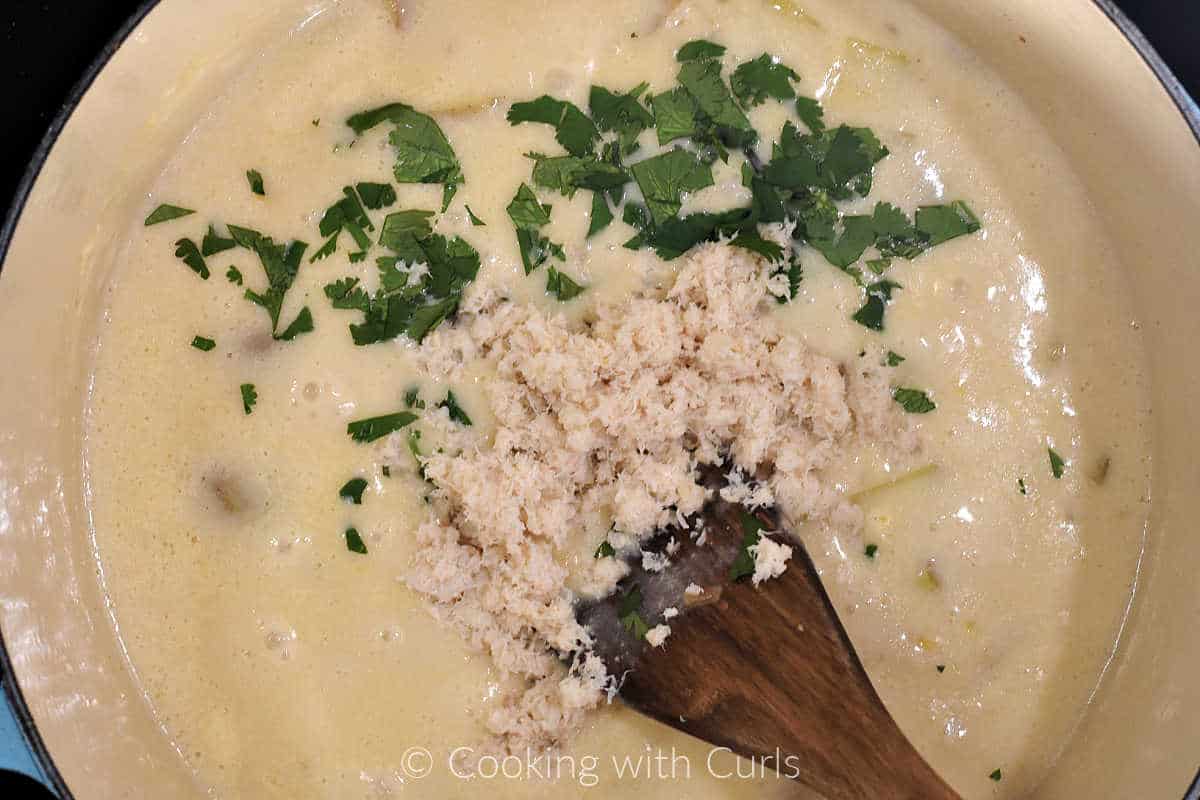 Chopped cilantro and crab meat sitting on top of the cooked chowder in a large pot. 