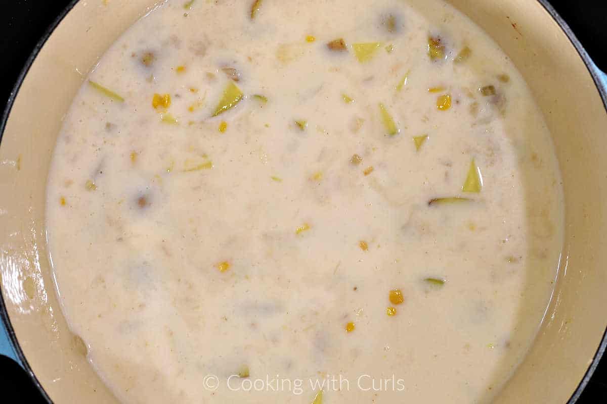 Cooked chowder with potatoes, corn, onion, seafood stock, and milk in a large pot. 