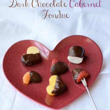 Dark Chocolate Cabernet Fondue covered fruits and marshmallows siting on a red heart shaped plate.