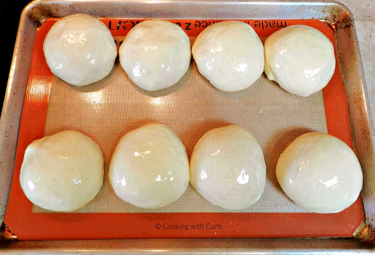 Eight dough balls on a silicone lined baking sheet.
