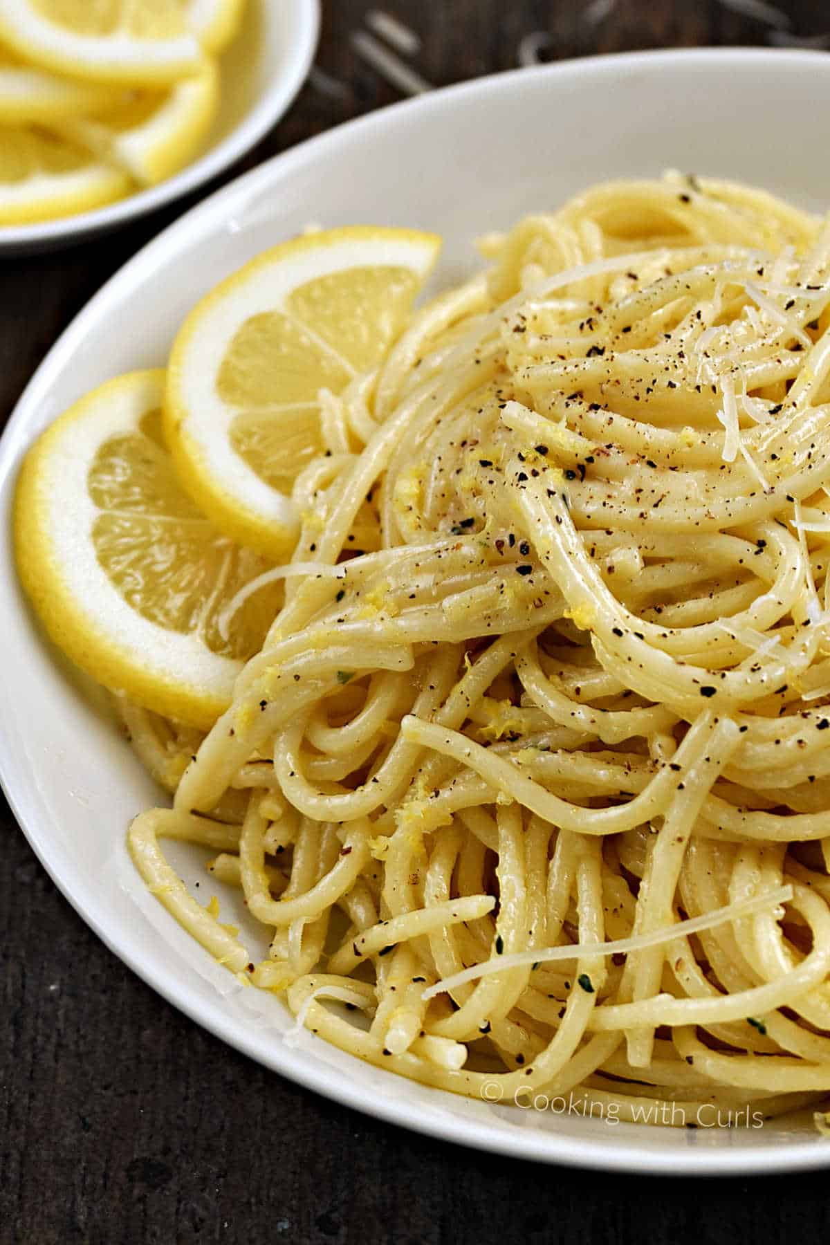 Spaghetti with lemon sauce in a bowl with lemon slices and sprinkled with black pepper.