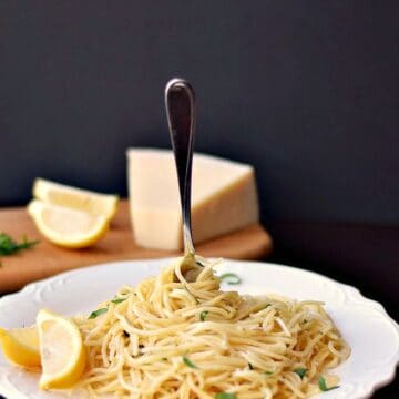 spaghetti noodles swirled on a white plate with a fork stuck in the middle and a wedge of parmesan in the background
