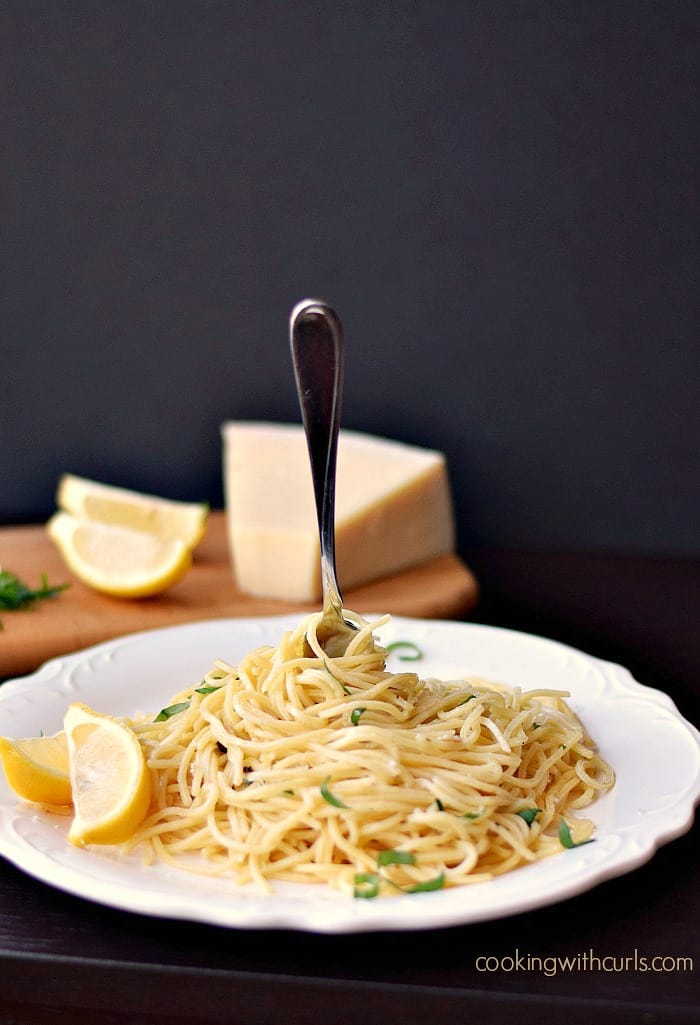 spaghetti noodles swirled on a white plate with a fork stuck in the middle and a wedge of parmesan in the background