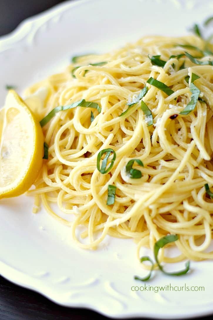 spaghetti noodles on a white plate garnished with a lemon wedge and chopped parsley