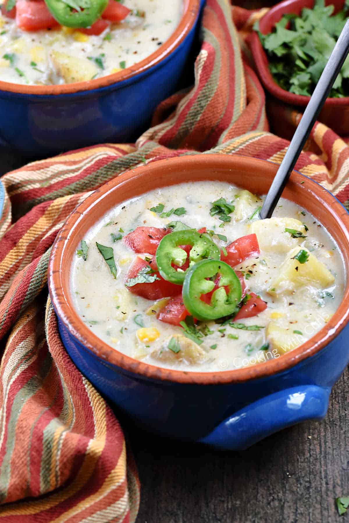 Two bowls of Southwest Crab Chowder with chopped tomato, sliced jalapeno and cilantro sitting on a striped napkin. 