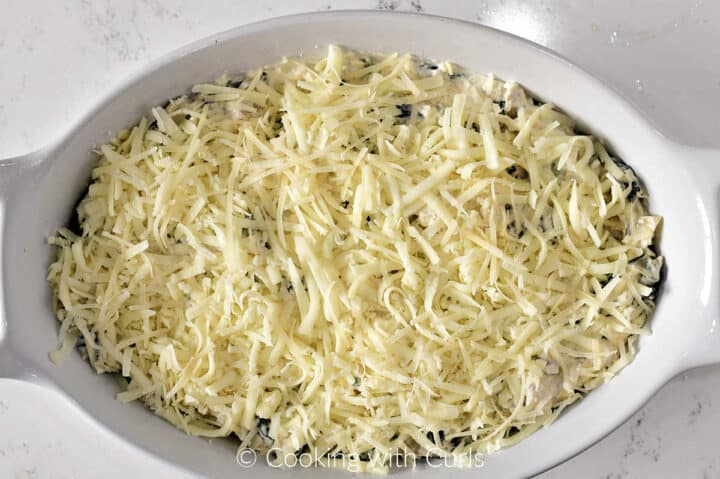 An oval baking dish filled with creamy spinach artichoke dip topped with grated mozzarella cheese. 