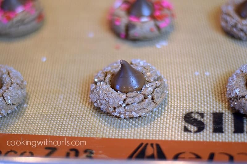 Chocolate candy kisses pressed into the center of the warm cookies on a silicone lined baking sheet.