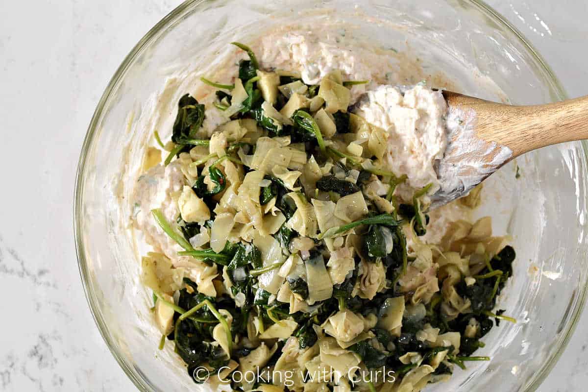 Chopped artichokes and spinach on top of the cream cheese mixture in a large mixing bowl. 