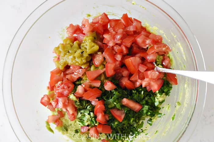 Chopped tomatoes, cilantro, and chiles in a glass bowl with mashed avocado. 