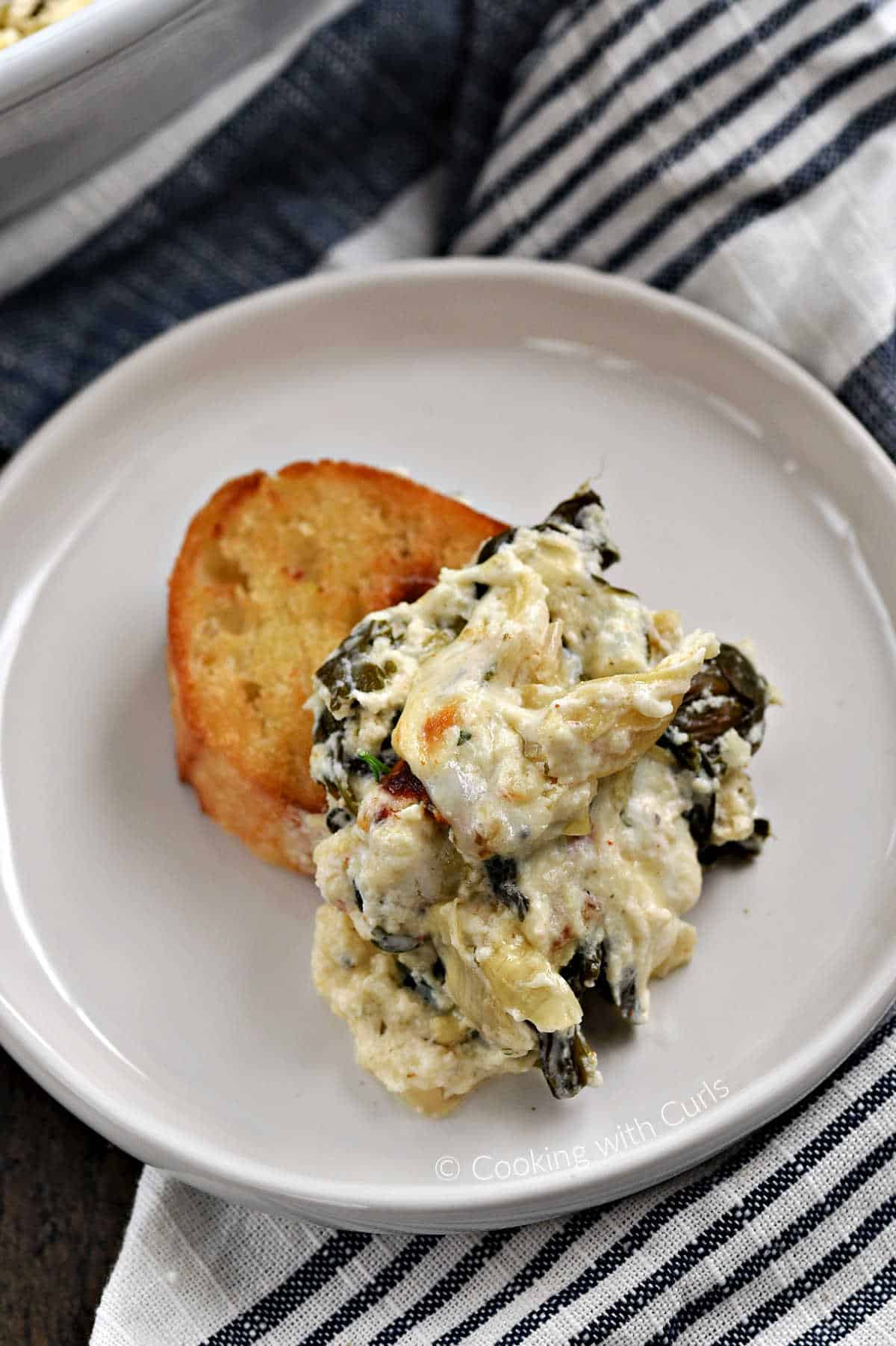 Creamy Spinach Artichoke scooped out onto a crostini sitting on a small plate. 