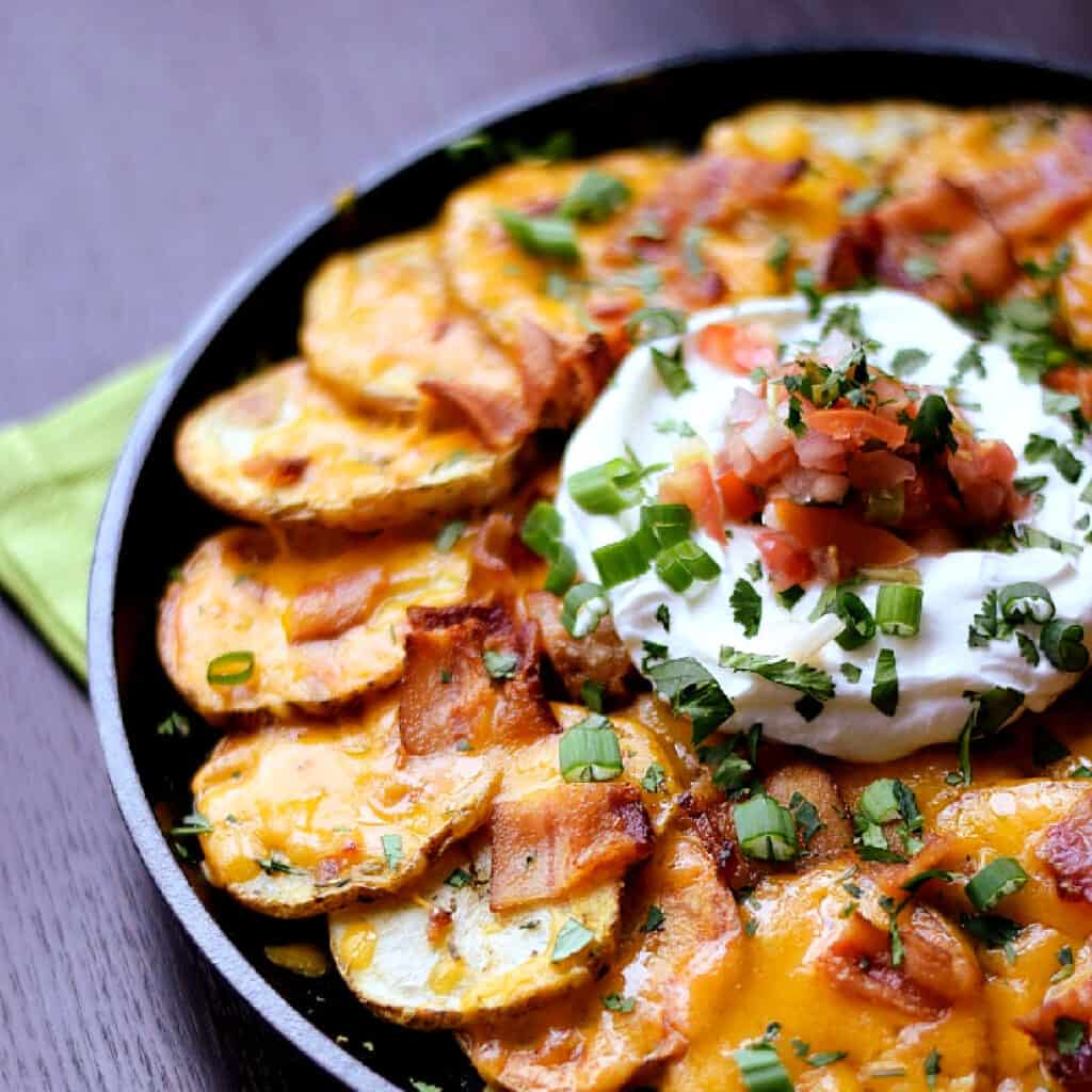 Thinly sliced potatoes arranged in a cast iron skillet topped with melted cheese, bacon, sour cream, salsa and green onions.
