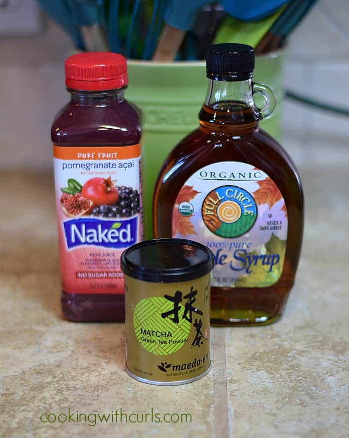 A bottle of fruit juice, maple syrup and small can of matcha green tea powder on the counter.