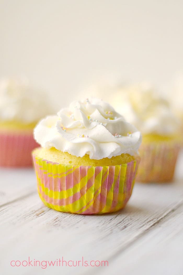 white frosting topped cupcakes in pink and yellow spring wrappers sitting on a white background