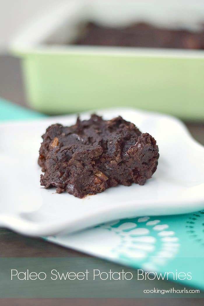 paleo sweet potato brownie on a square white plate with a green baking dish in the background