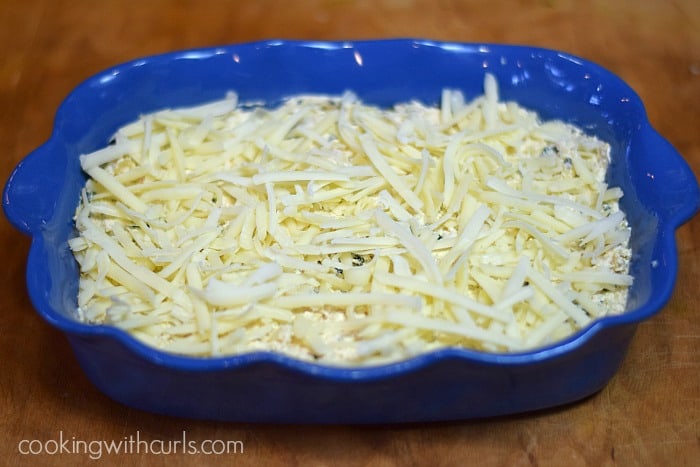cheese topped dip in a bright blue baking dish sitting on a wood board