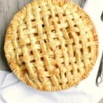 lattice top apple pie on a wood table with a white towel and silver pie server on the side