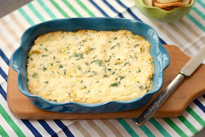 Thick and creamy Spinach Artichoke Dip in a dark blue baking dish sitting on a wooden board