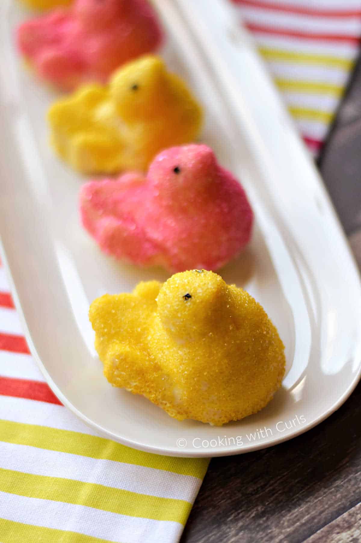 Pink and yellow sprinkle covered chicks on an oval platter sitting on a pink, yellow and white striped napkin.