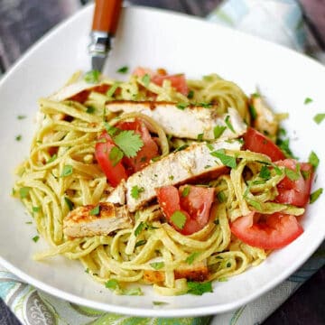 A bowl of Guacamole Linguine with Chicken topped with chopped tomatoes and parsley.