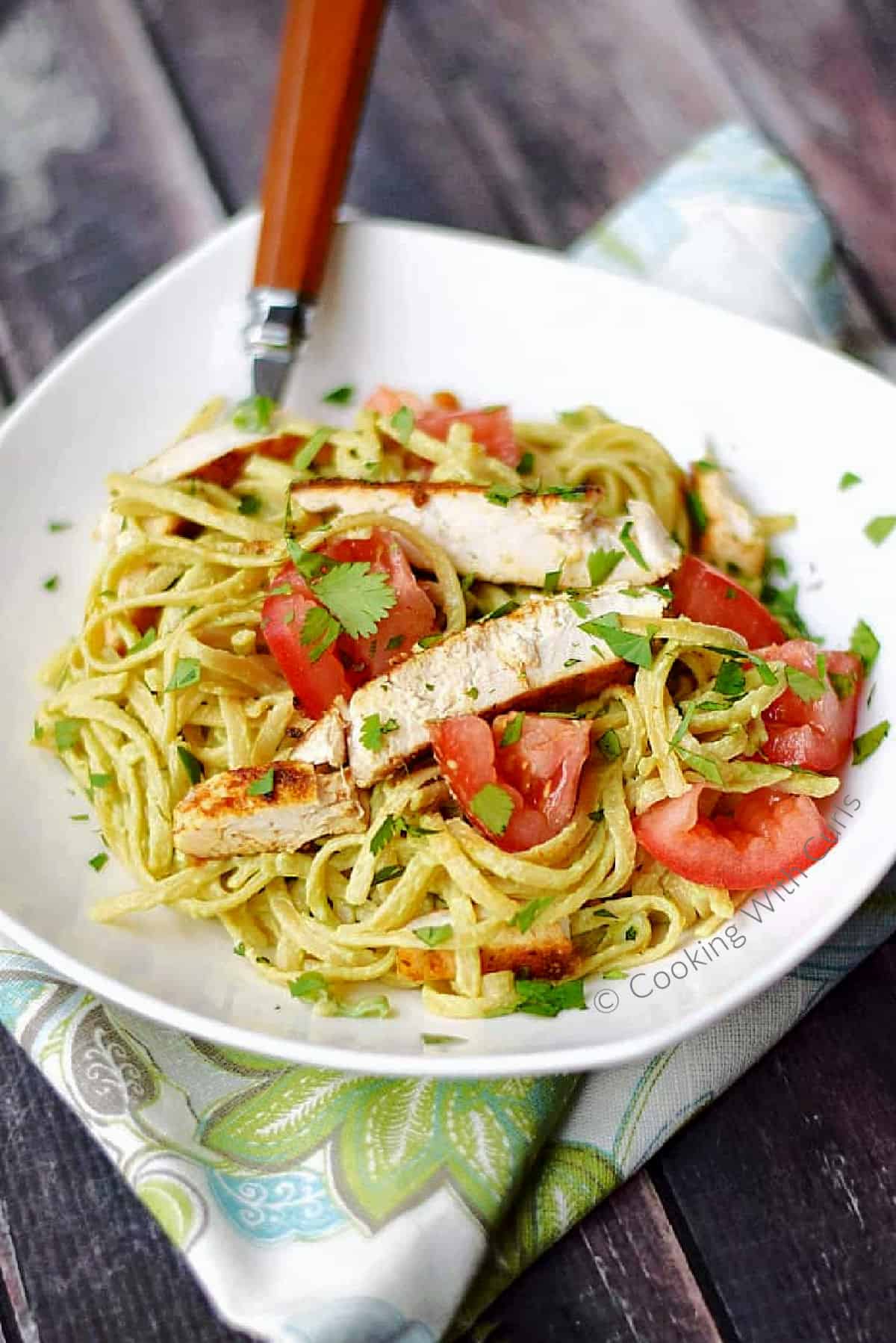 A bowl of Guacamole Linguine with Chicken topped with chopped tomatoes and parsley. 